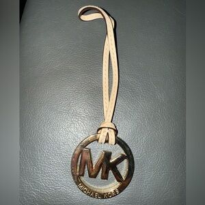 Michael Kors Gold Tone MK Logo Charm With A Light Tan/Creme Color Leather Tassel